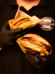 Équipier en gants noirs présentant deux burgers Tonton Chami emballés